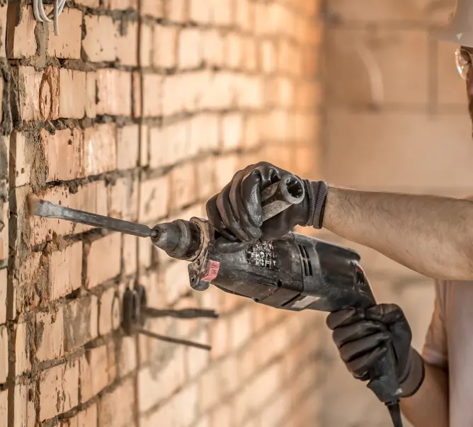 Outil électrique en train de démolir un mur en brique à l’intérieur d’un bâtiment