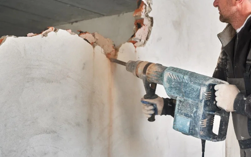 Ouvrier en train de démolir un mur intérieur à l’aide d’un marteau-piqueur.
